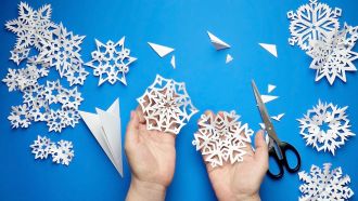 Close up on hands making paper snowflakes.