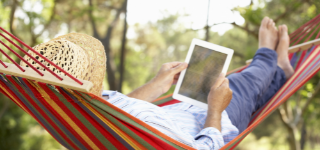 Person in a sunhat relaxing in a hammock and reading on their tablet.