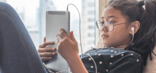 A girl wearing earbuds is looking at her tablet